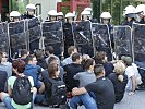 Sitzende Demonstranten blockieren Fahrtstrecke des Konvois. (Bild öffnet sich in einem neuen Fenster)
