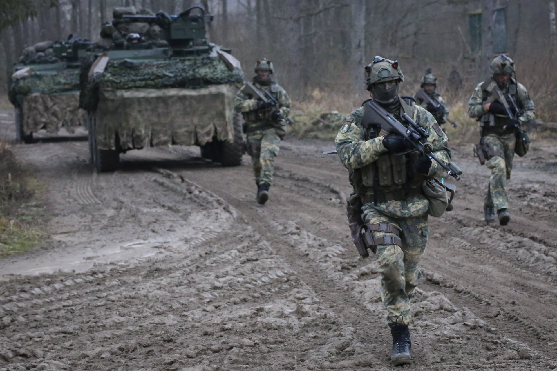 Soldaten laufen vor einem Radpanzer