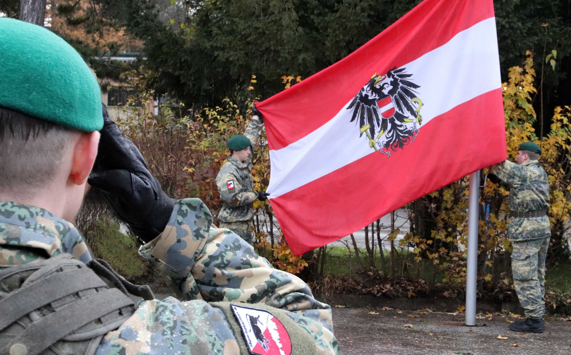 Ein Soldat salutiert vor der österreichischen Fahne.