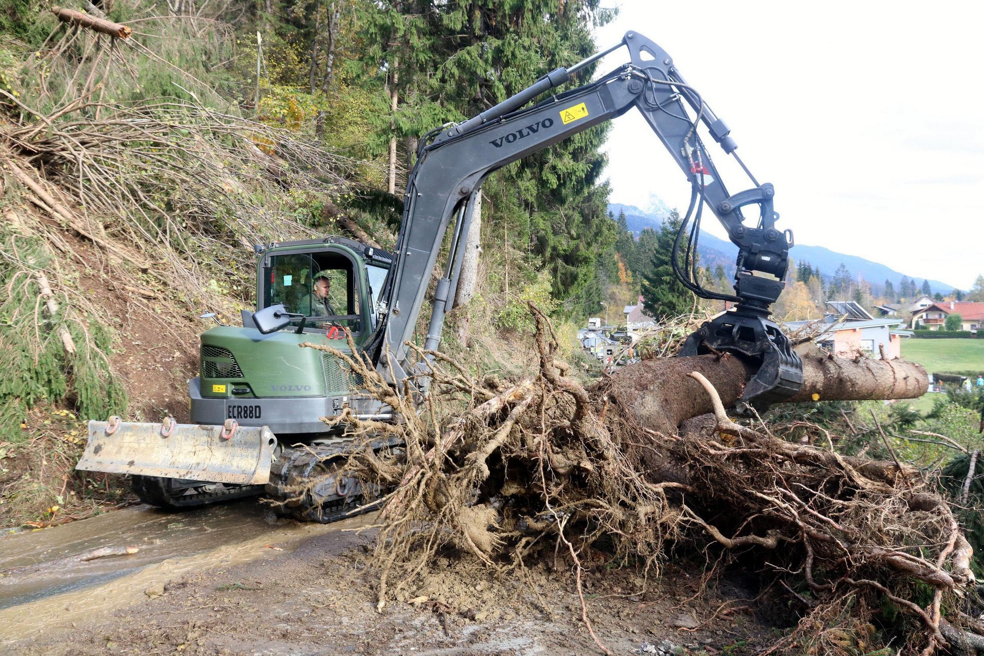 Ein Bagger räumt einen umgefallenen Baumstamm von der Straße 