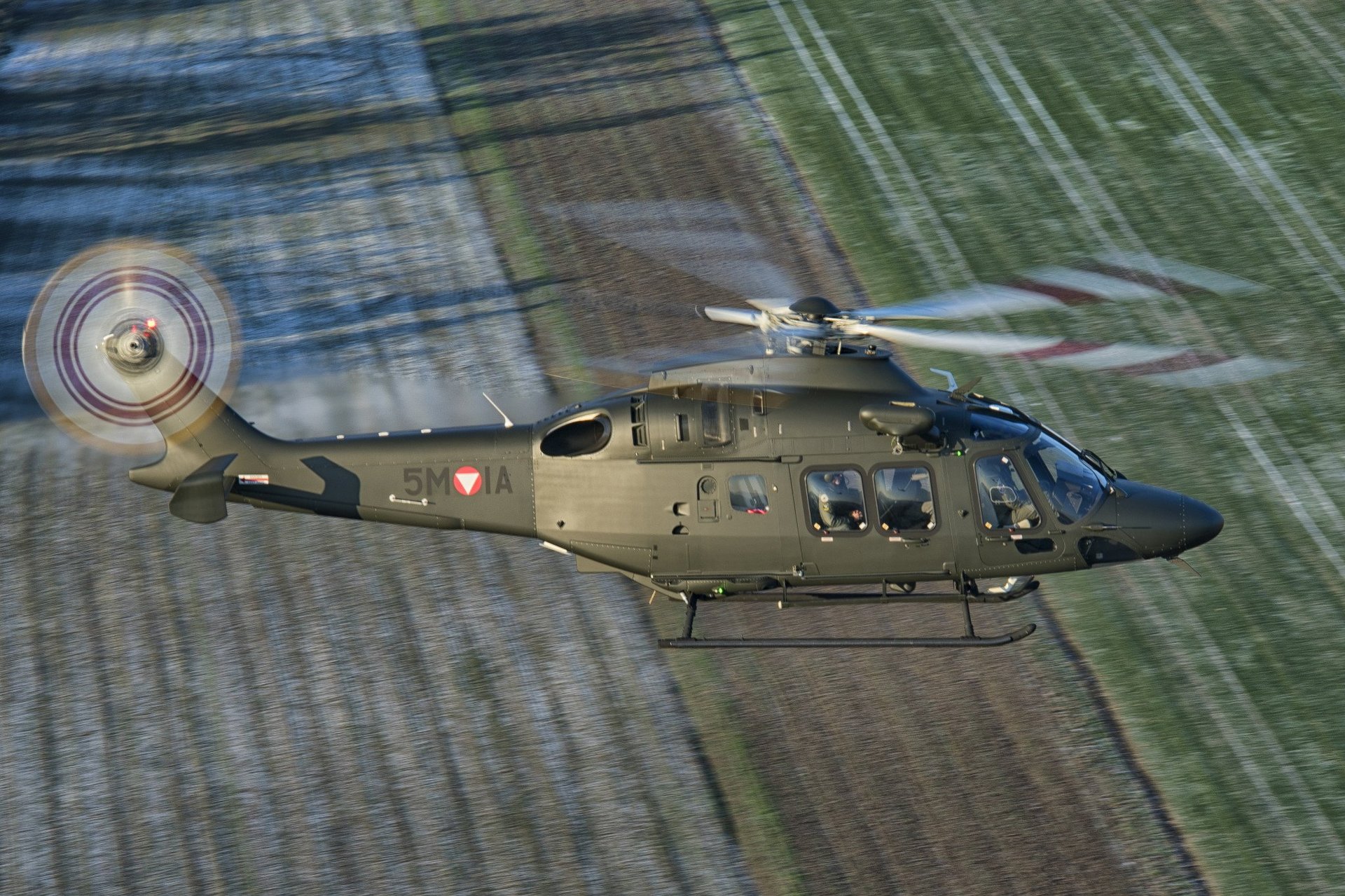 Ein AW-169 "Lion" Hubschrauber fliegt über ein Feld.